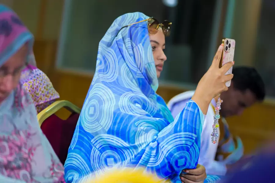 Melhfa à motifs bleus, téléphone levé : elle filme la scène à son tour.