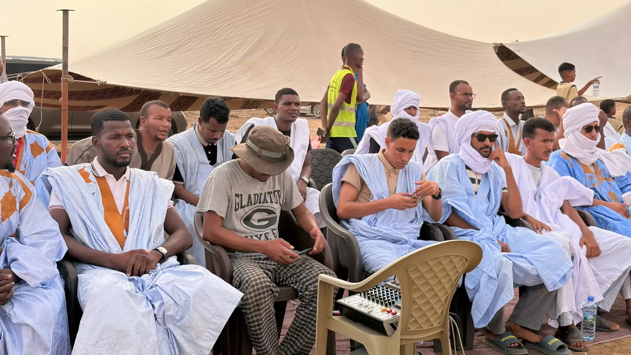 Le public, en daraa bleue et blanche, suit la cérémonie à l’ombre.
