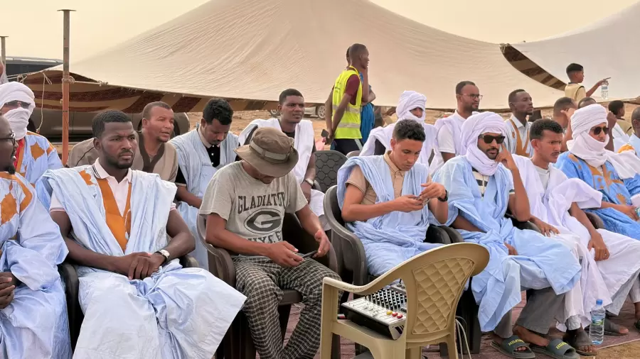 Le public, en daraa bleue et blanche, suit la cérémonie à l’ombre.