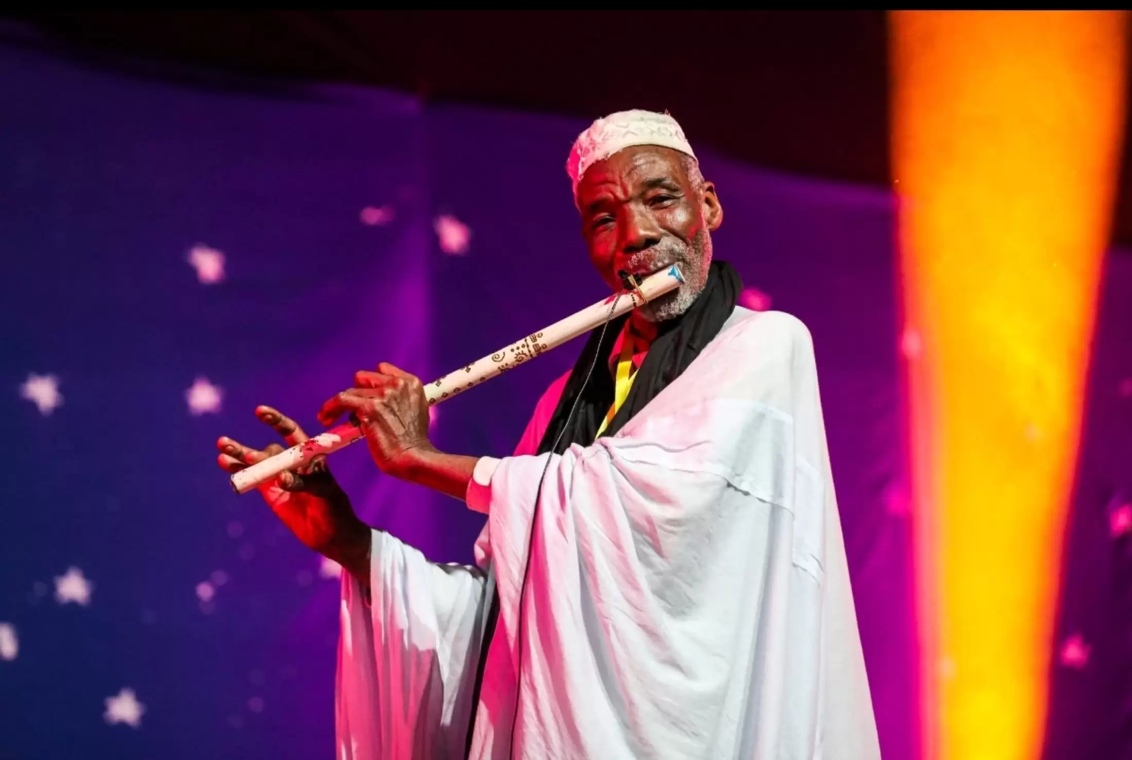 Un musicien joue de la flûte dans la lumière violette de la scène.