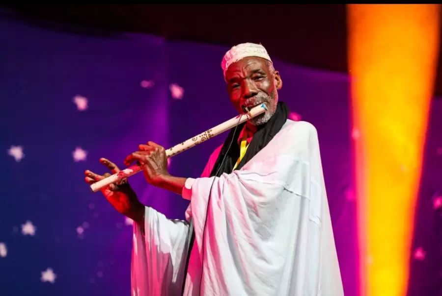 Un musicien joue de la flûte dans la lumière violette de la scène.