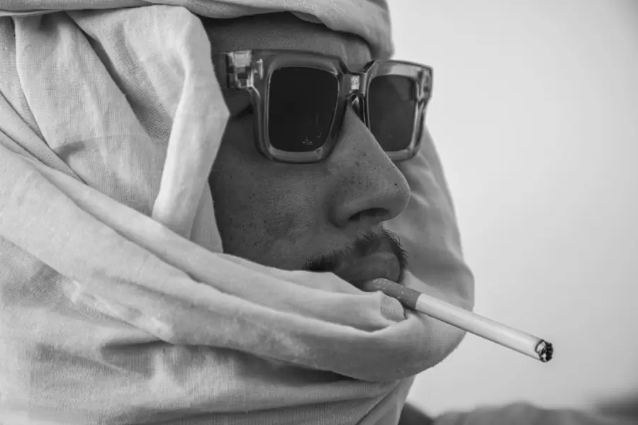 Chèche blanc, lunettes noires, cigarette aux lèvres : un portrait tout en contraste.